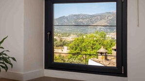A room with a large window offering a view of a mountainous landscape and a village below.