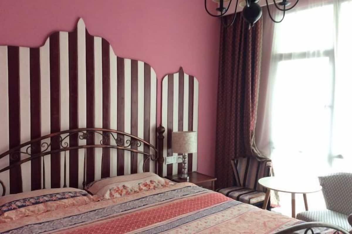A bedroom with a striped headboard, a bed with patterned bedding, a bedside lamp, a chair, and a small table.