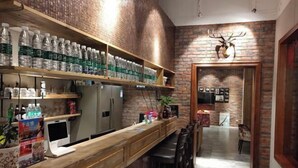 A bar area with a long counter, shelves with bottled water, a refrigerator, and a mounted deer head decoration.