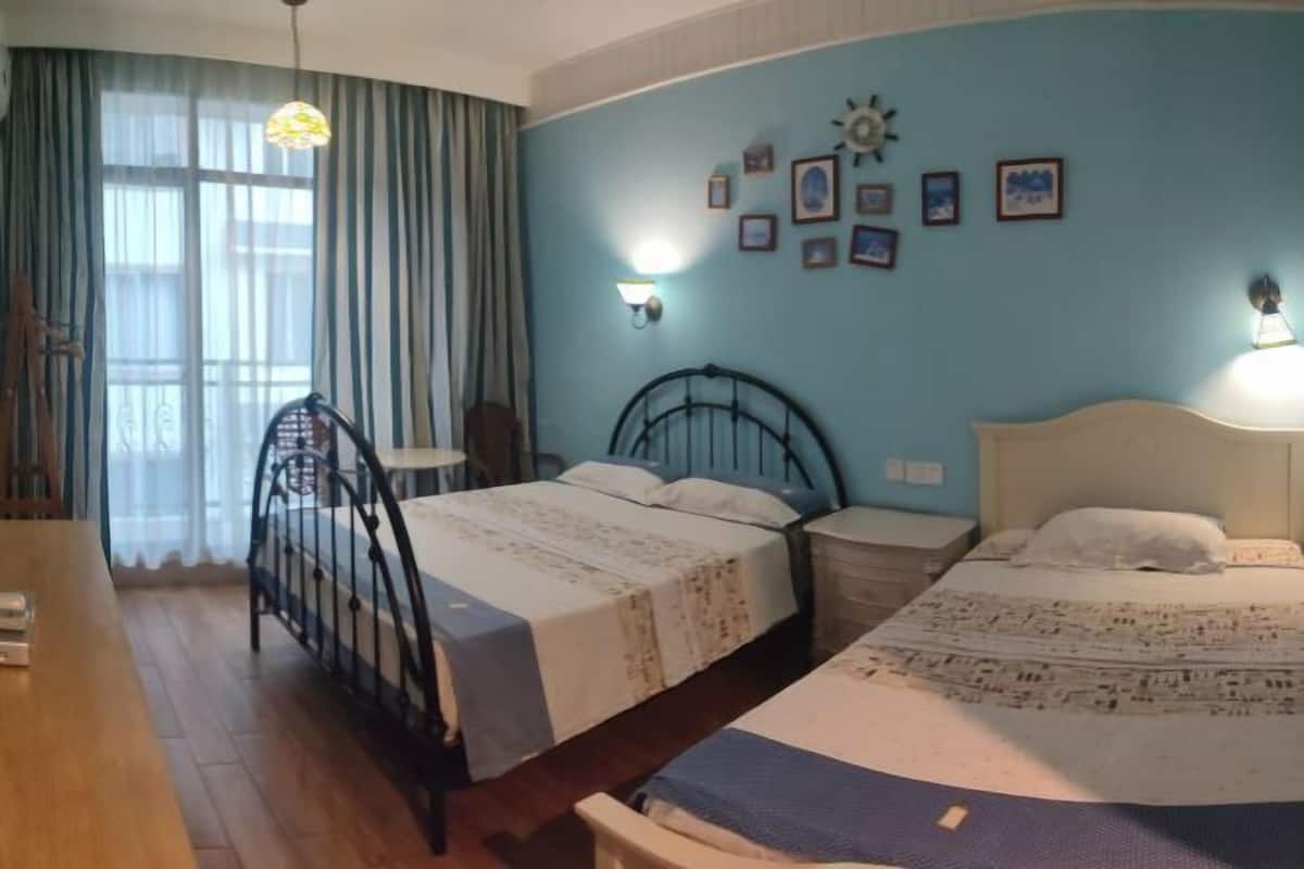A bedroom with two beds, a wooden floor, a window with curtains, and wall-mounted lights.