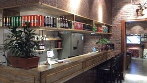 A bar area with shelves stocked with beverages, a computer monitor, and a potted plant.