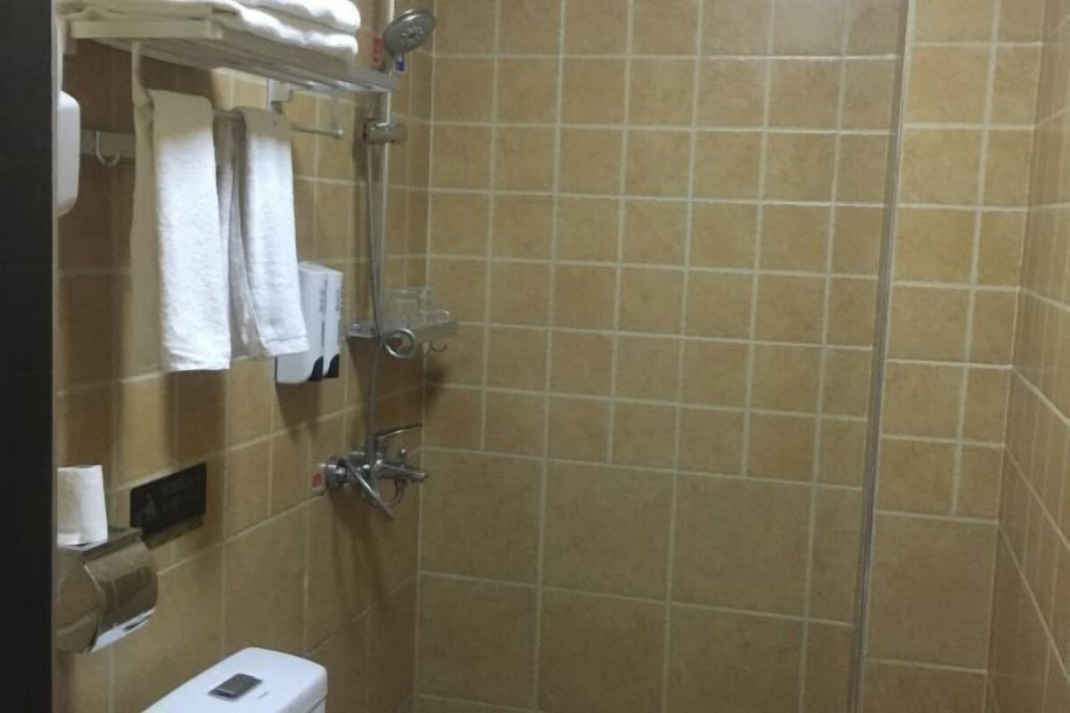 A bathroom with beige tiles, a toilet, a towel rack, and a shower area.
