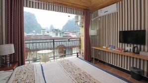 A hotel room with a bed, a TV, a small table, and a balcony with a view of mountains.