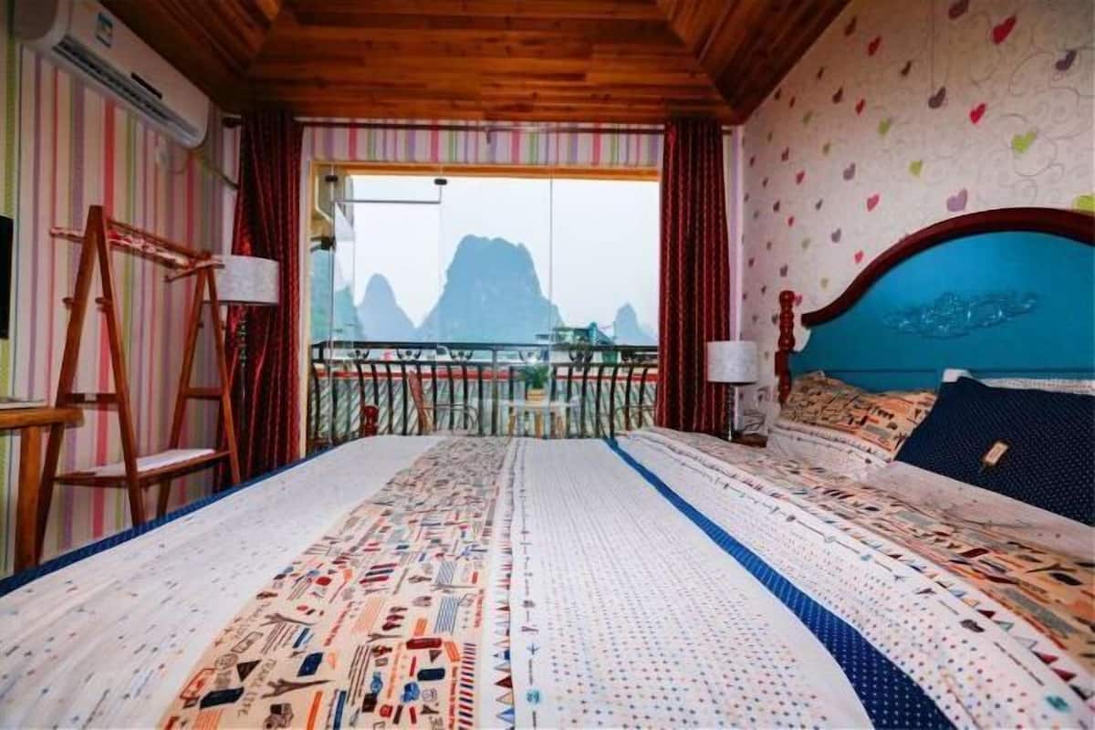 A bedroom with a large bed, a wooden headboard, a view of mountains through a balcony, and striped walls.
