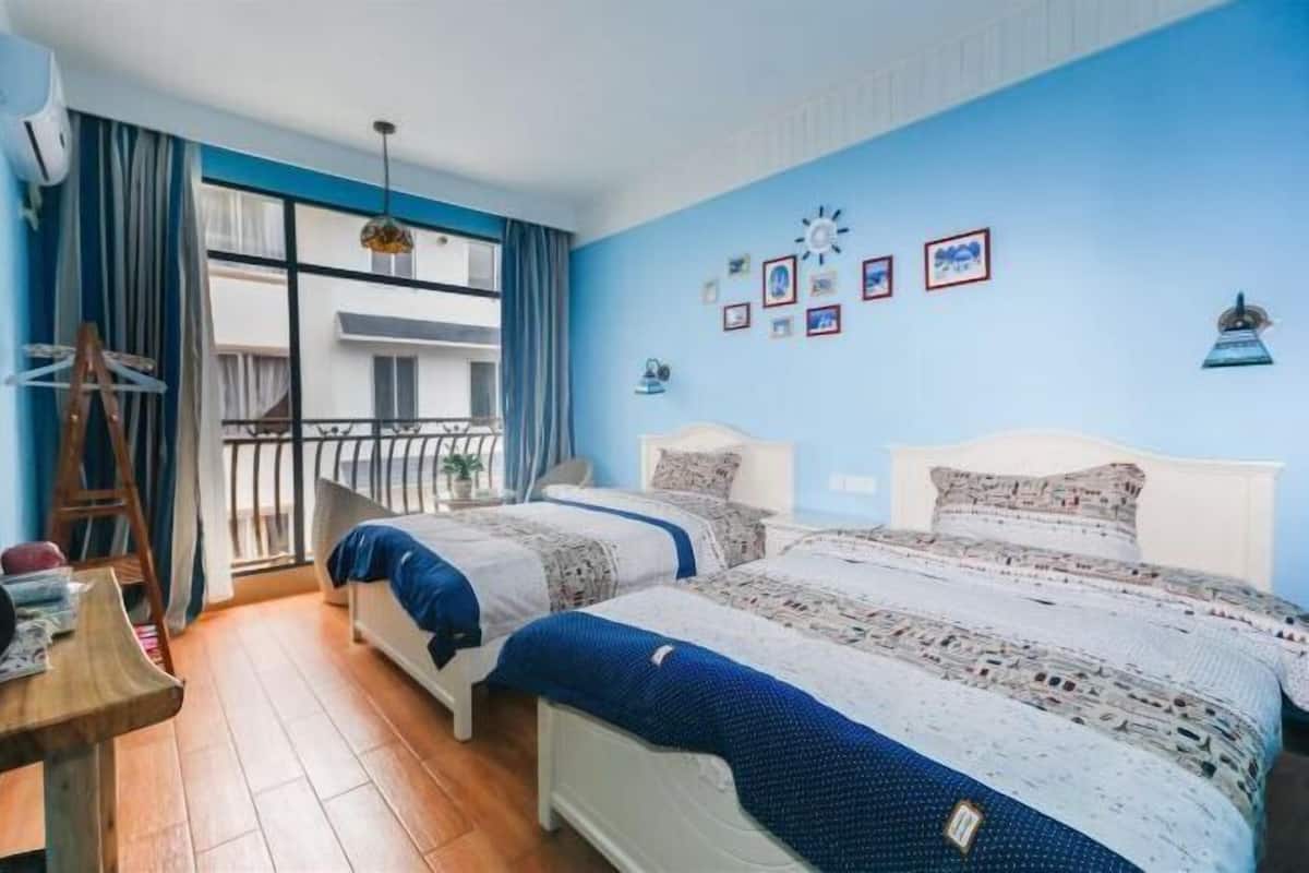 A bedroom with two beds, a balcony, a wooden table, and a blue wall.