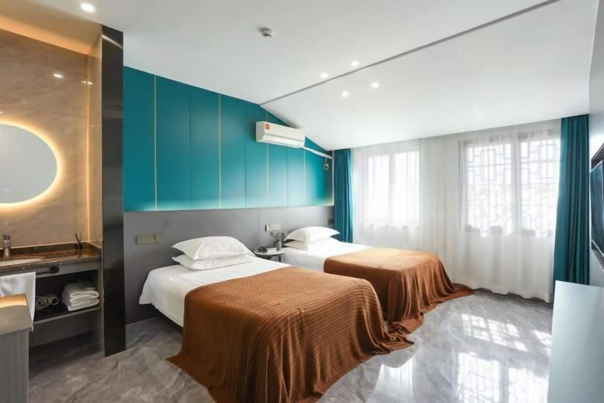 Ein Hotelzimmer mit zwei Betten, einem Badezimmer mit Spiegel und Waschbecken sowie einem großen Fenster mit Vorhängen.