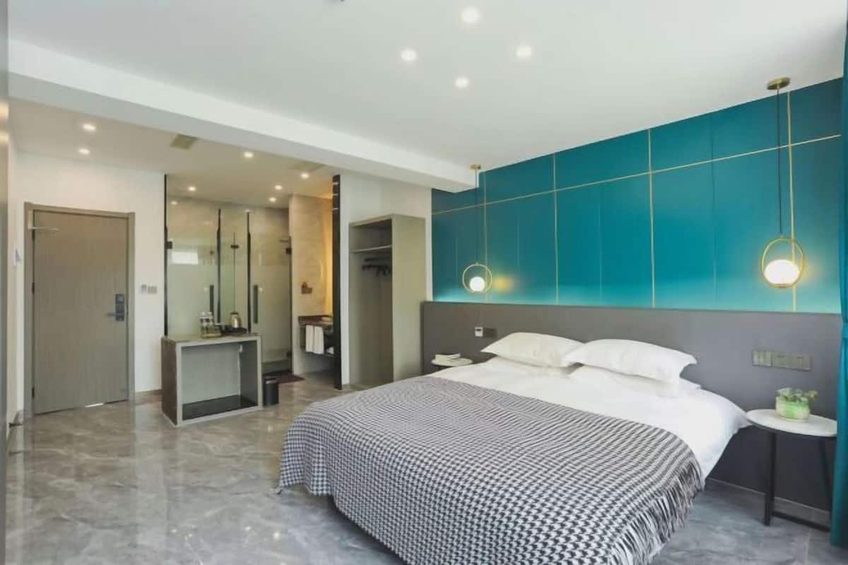 Ein modernes Hotelzimmer mit einem großen Bett, einem Schreibtisch, einem Spiegel und einem durch eine offene Tür einsehbaren Badezimmer.