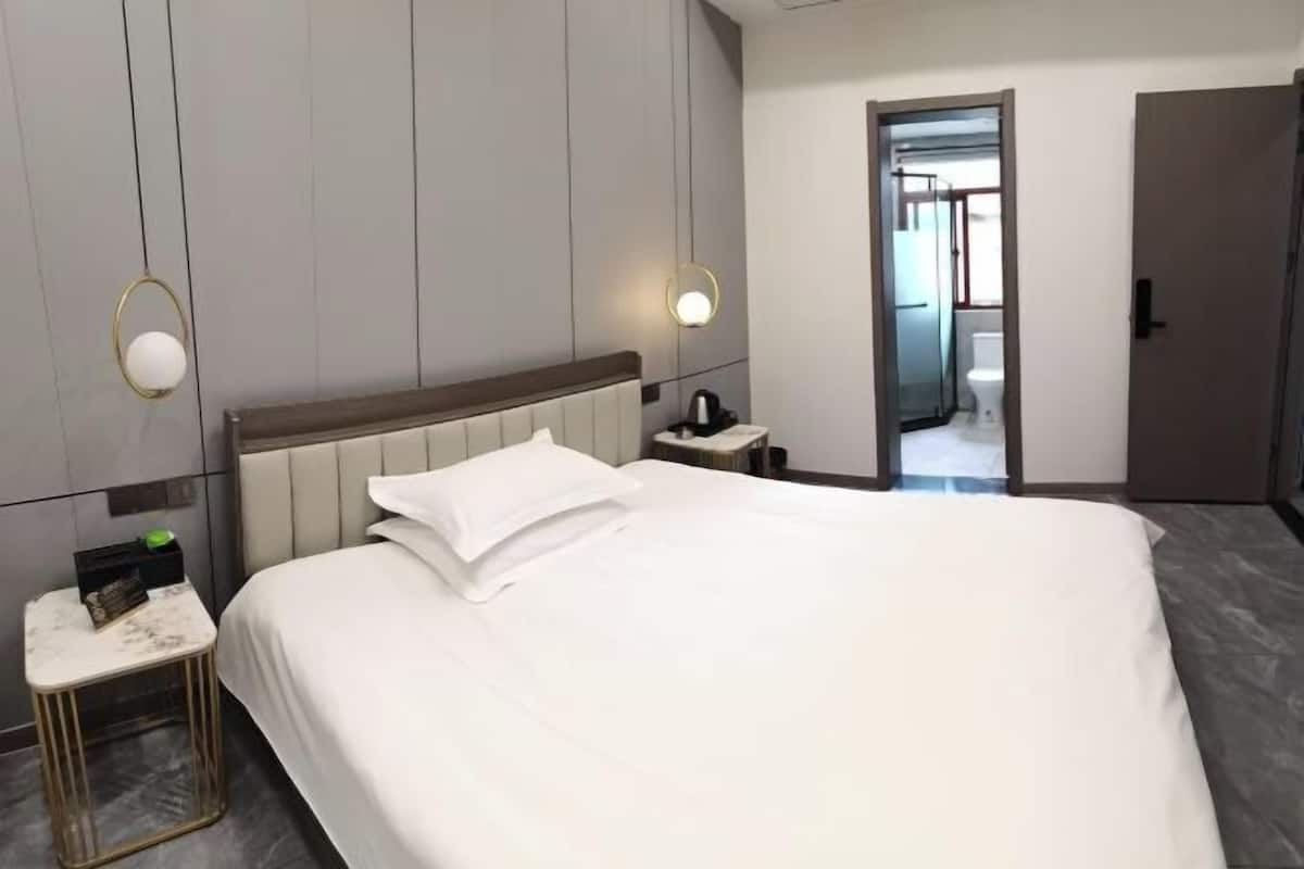 Ein Hotelzimmer mit einem großen Bett, einem Nachttisch und einem Beistelltisch. Eine Tür führt zu einem Badezimmer und einem Flur.