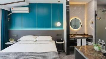 Una habitación de hotel moderna con una cama grande, un espejo redondo, un baño con lavamanos y ducha, y paredes color turquesa.