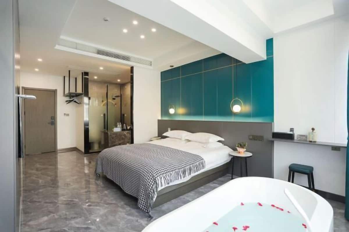 Ein modernes Hotelzimmer mit einem großen Bett, einer Badewanne mit Rosenblättern, einem kleinen runden Tisch und einem Spiegel.