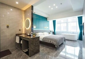 Una habitación de hotel moderna con baño de mármol, una cama grande, baño independiente y un amplio ventanal con cortinas.