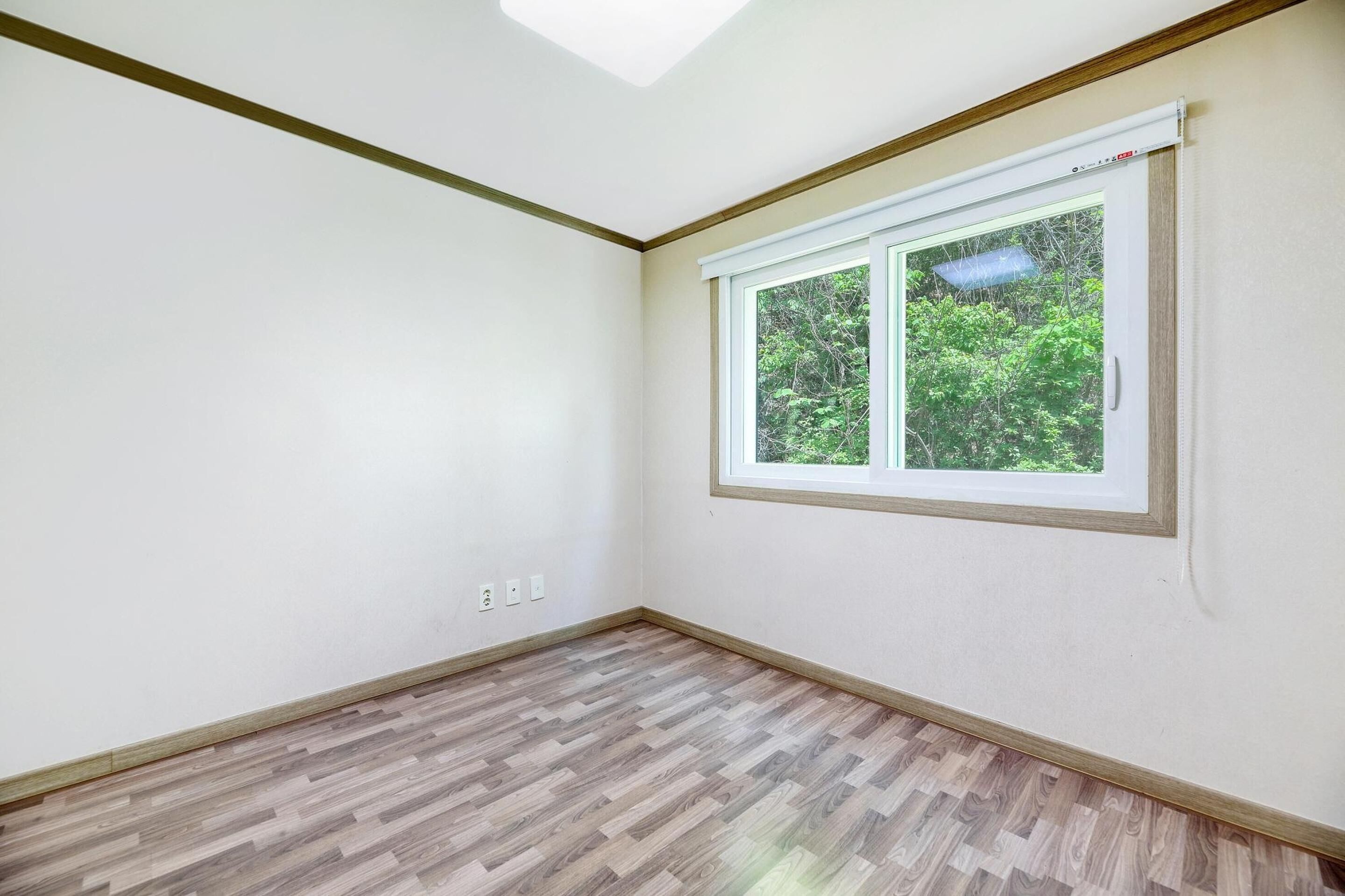 A room with a large window, wooden flooring, and white walls.