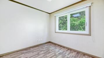 A room with a large window, wooden flooring, and white walls.