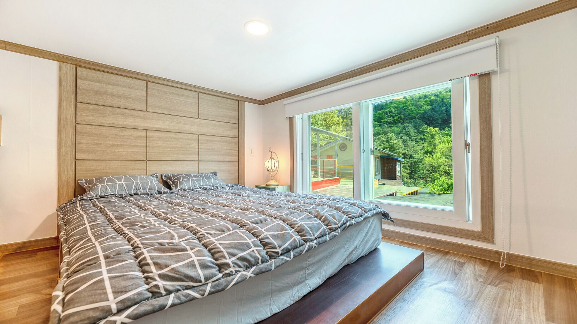 Un dormitorio moderno con una cama grande, cabecera de madera y puerta de cristal corredera que da a un balcón.
