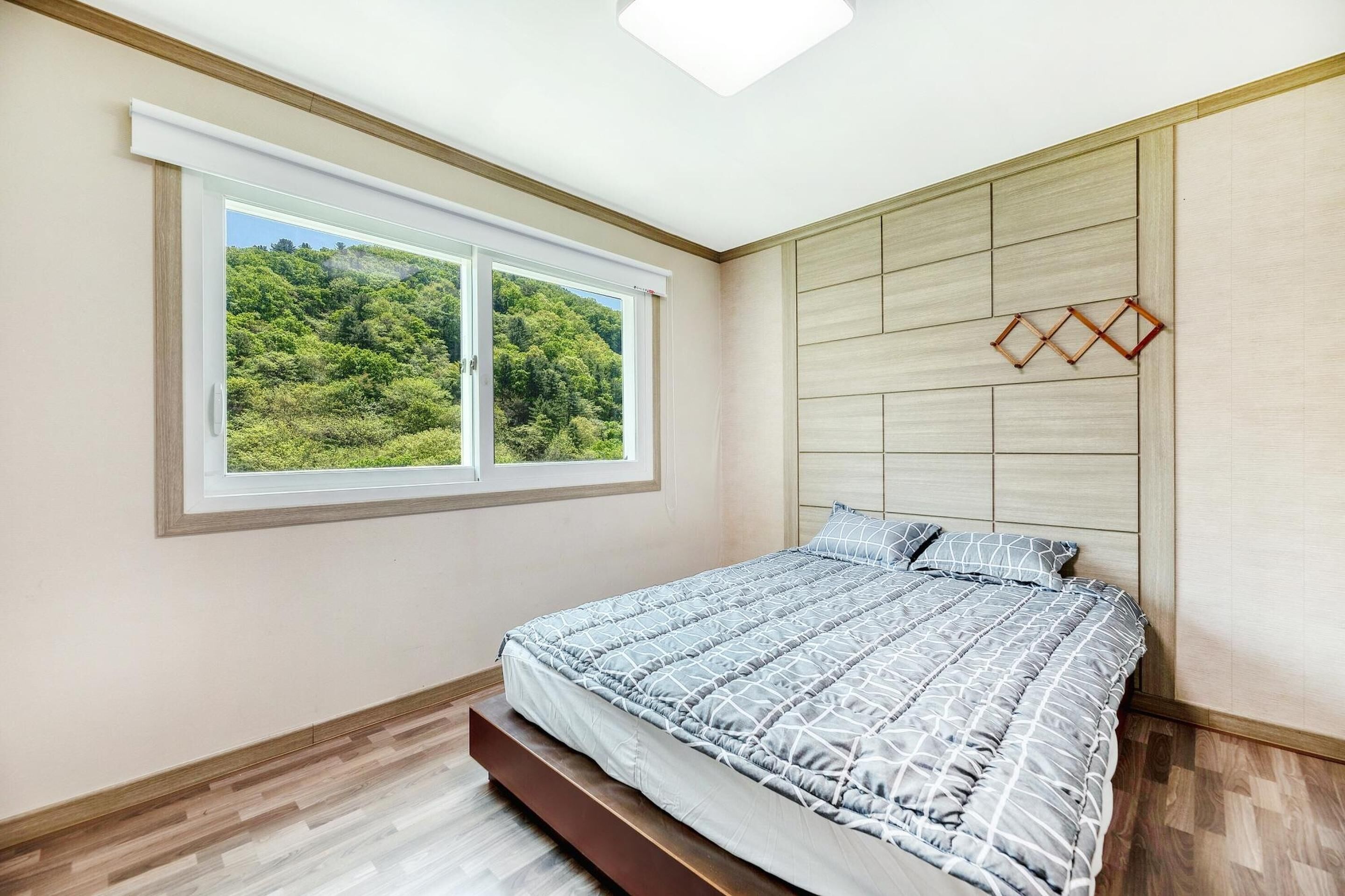 A bedroom with a bed, a window with a view of greenery, and a wooden headboard.