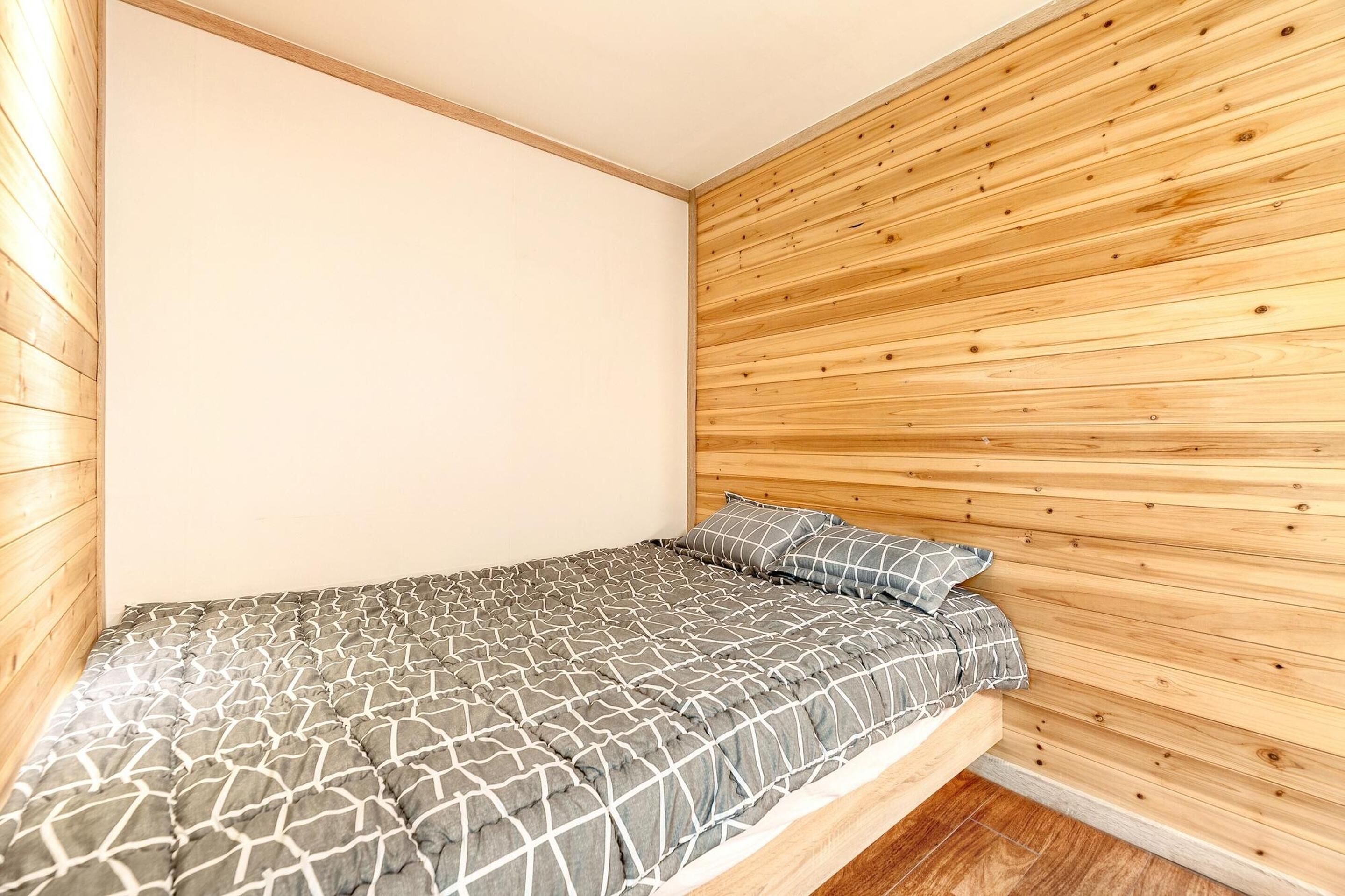 A single bed with a geometric-patterned bedspread in a room with wooden panel walls and a white ceiling.