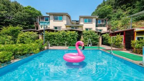 A swimming pool with a pink flamingo float, surrounded by greenery and buildings.