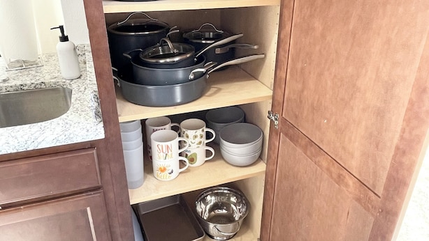 A kitchen with wooden cabinets, a granite countertop, and various kitchenware including pots, pans, and mugs. - Spacious 4-bedroom house in enjoyable Pensacola with AC, WiFi (Pensacola)