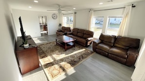 A spacious living room with a brown leather sofa, a wooden coffee table, and a large window providing a view of the outdoors. - Spacious 4-bedroom house in enjoyable Pensacola with AC, WiFi (Pensacola)