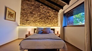 A bedroom with a stone wall, a bed with pillows, bedside lamps, and a window with curtains. - YourHouse O Canton villa (Ourense)