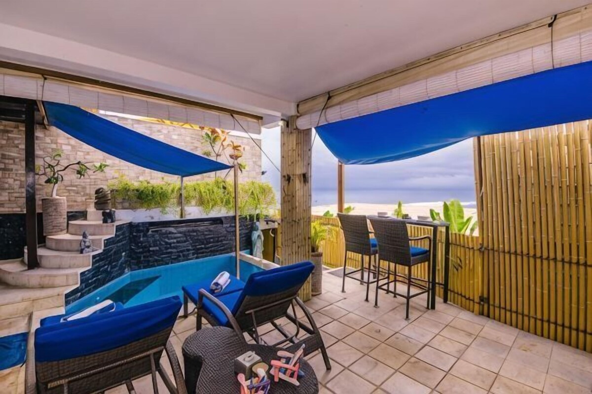 A covered outdoor area with a pool, seating, and a view of the sea.