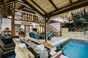 A poolside area with a dining table set for four, a staircase, and a pool. - Lembongan Harmony Villas (Bali)