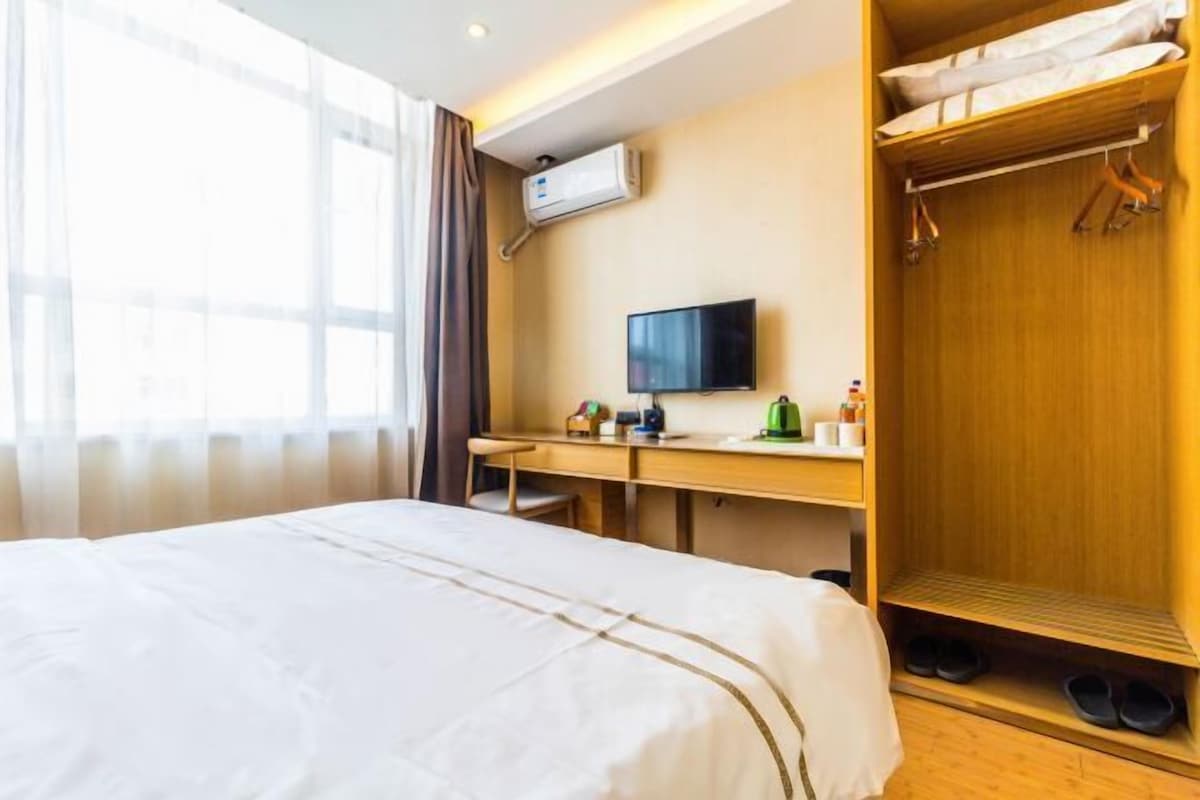 A hotel room with a bed, a desk, a television, and a wardrobe.