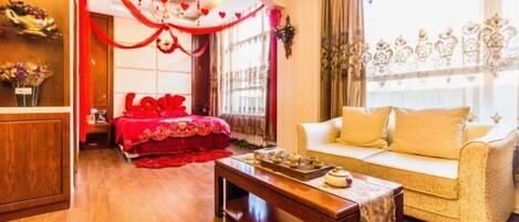 A room with a bed, a sofa, a wooden coffee table, and a window with curtains.