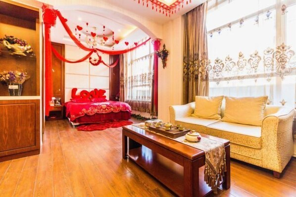A room with a bed, a sofa, a wooden coffee table, and a window with curtains.
