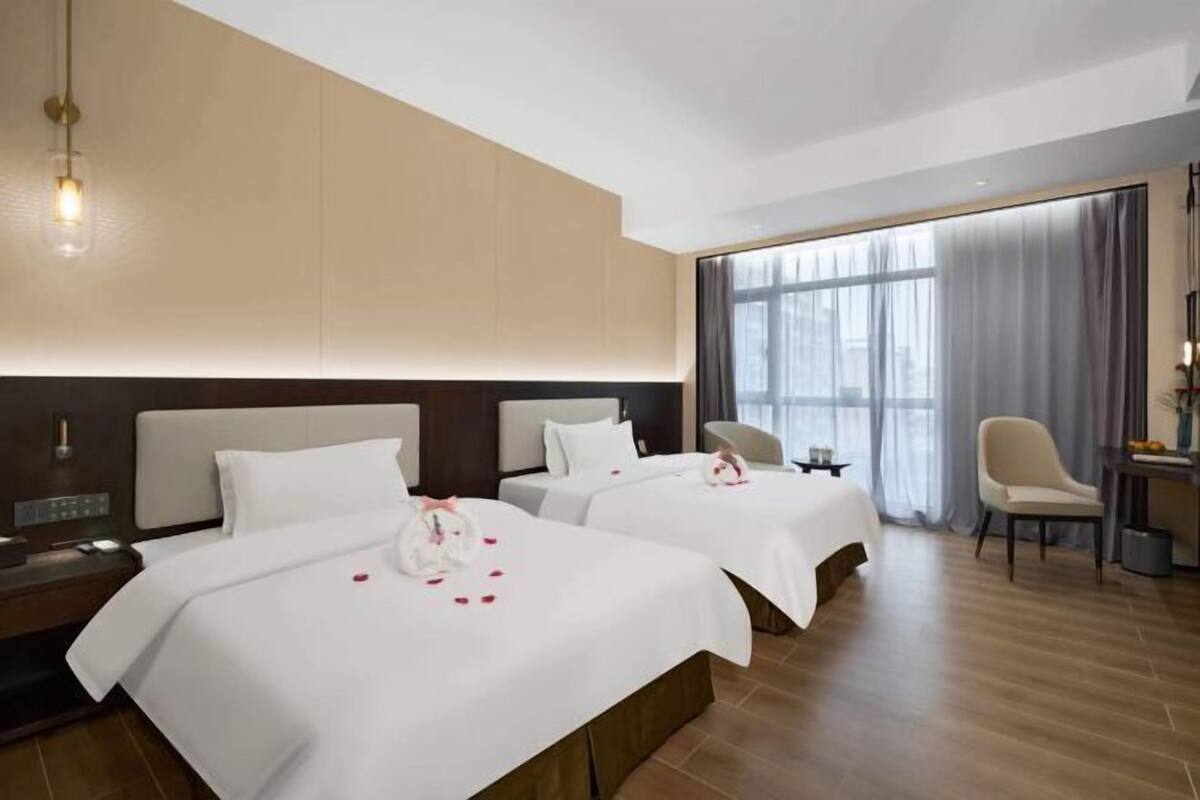 Een hotelkamer met twee bedden, een bureau, een stoel en een groot raam met gordijnen.