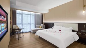 Een hotelkamer met een groot bed, een eettafeltje, een bank en een groot raam met gordijnen.