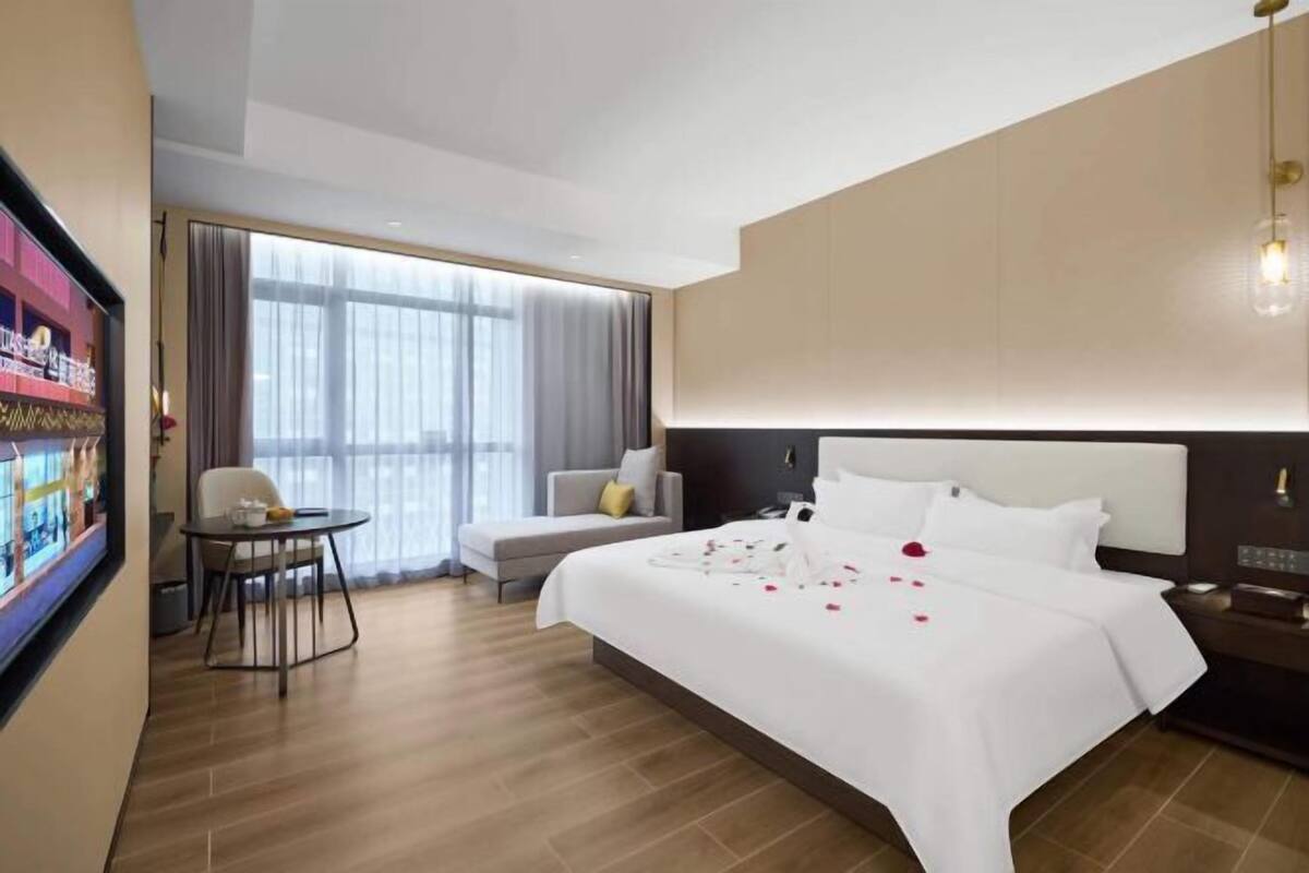 Een hotelkamer met een groot bed, een eettafeltje, een bank en een groot raam met gordijnen.