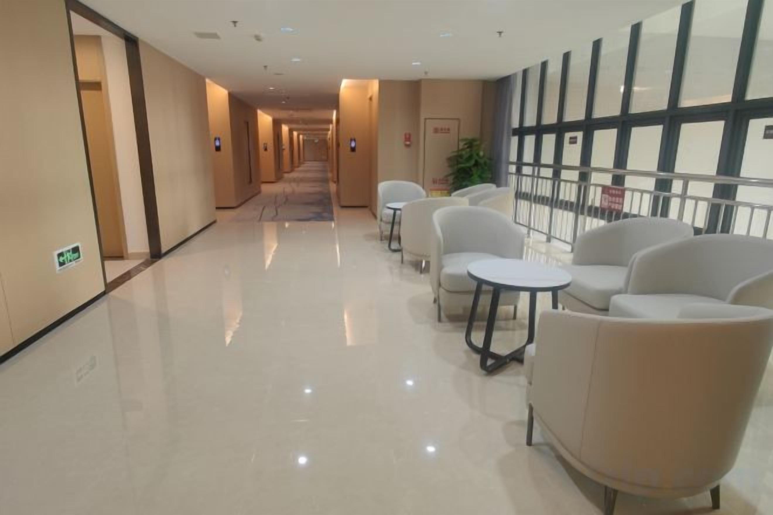 A hotel corridor with seating areas, a fire exit sign, and a view of the outside.