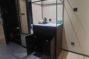 Une chambre d’hôtel avec un lit, une petite table, une bouilloire, une bouteille d’eau et une poubelle.