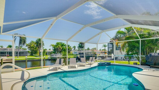A covered swimming pool with lounge chairs and a view of the waterway. - Holly's HomeAway-Private Pool, Kayaks & Canal Adventures (Cape Coral)