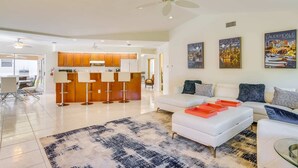 A spacious living area with a white sofa, a coffee table, and a patterned rug. There is a kitchen area with wooden cabinets and a white refrigerator. - Holly's HomeAway-Private Pool, Kayaks & Canal Adventures (Cape Coral)