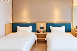 Een hotelkamer met twee bedden, een nachtkastje met een telefoon en een plant, en een groot raam.