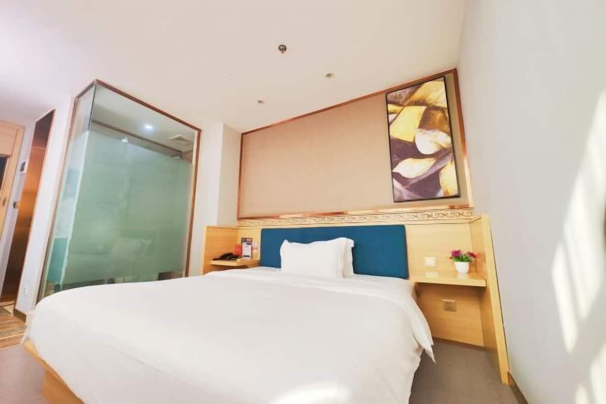 A hotel room with a large bed, a bedside table, a nightstand, a mirror, and a wall-mounted artwork.