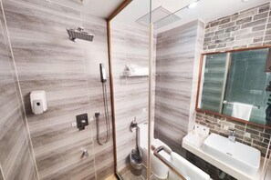 A modern bathroom with a glass shower enclosure, a white sink, and a mirror with a brick backsplash. - Yulai Hotel (Kunming)
