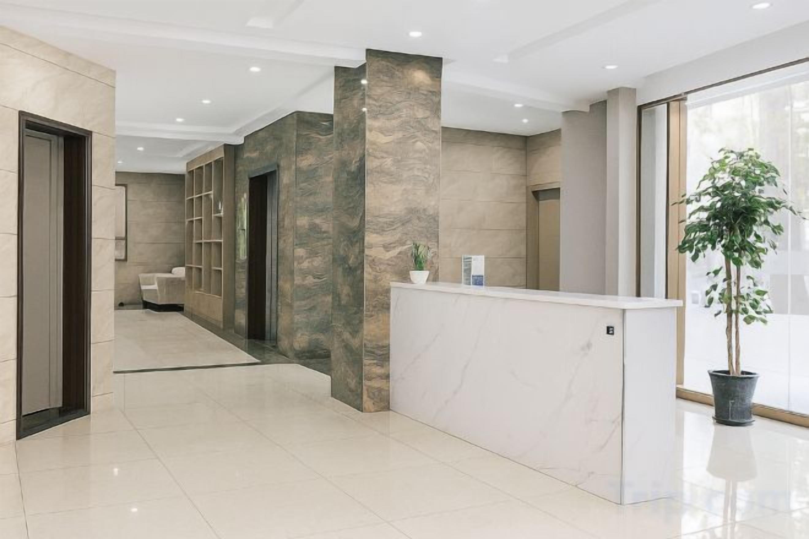 Zona de recepción de un hotel con un mostrador de mármol, una planta en maceta y un amplio ventanal que proporciona luz natural.