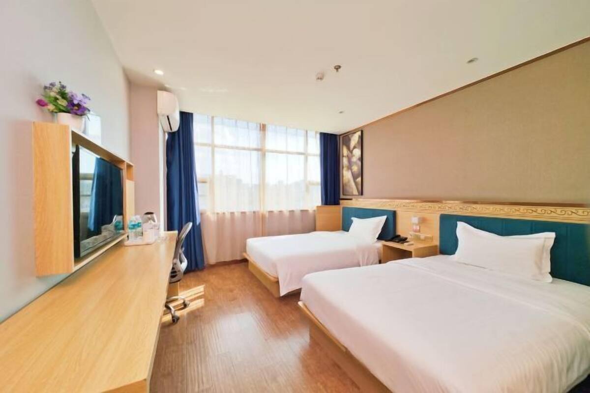 A hotel room with two beds, a TV, a desk, and a window with curtains.