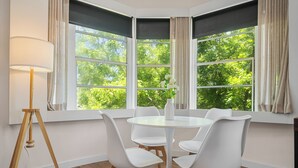 Ein Essbereich mit einem runden Tisch, weißen Stühlen, einer Stehlampe und großen Fenstern mit Vorhängen.