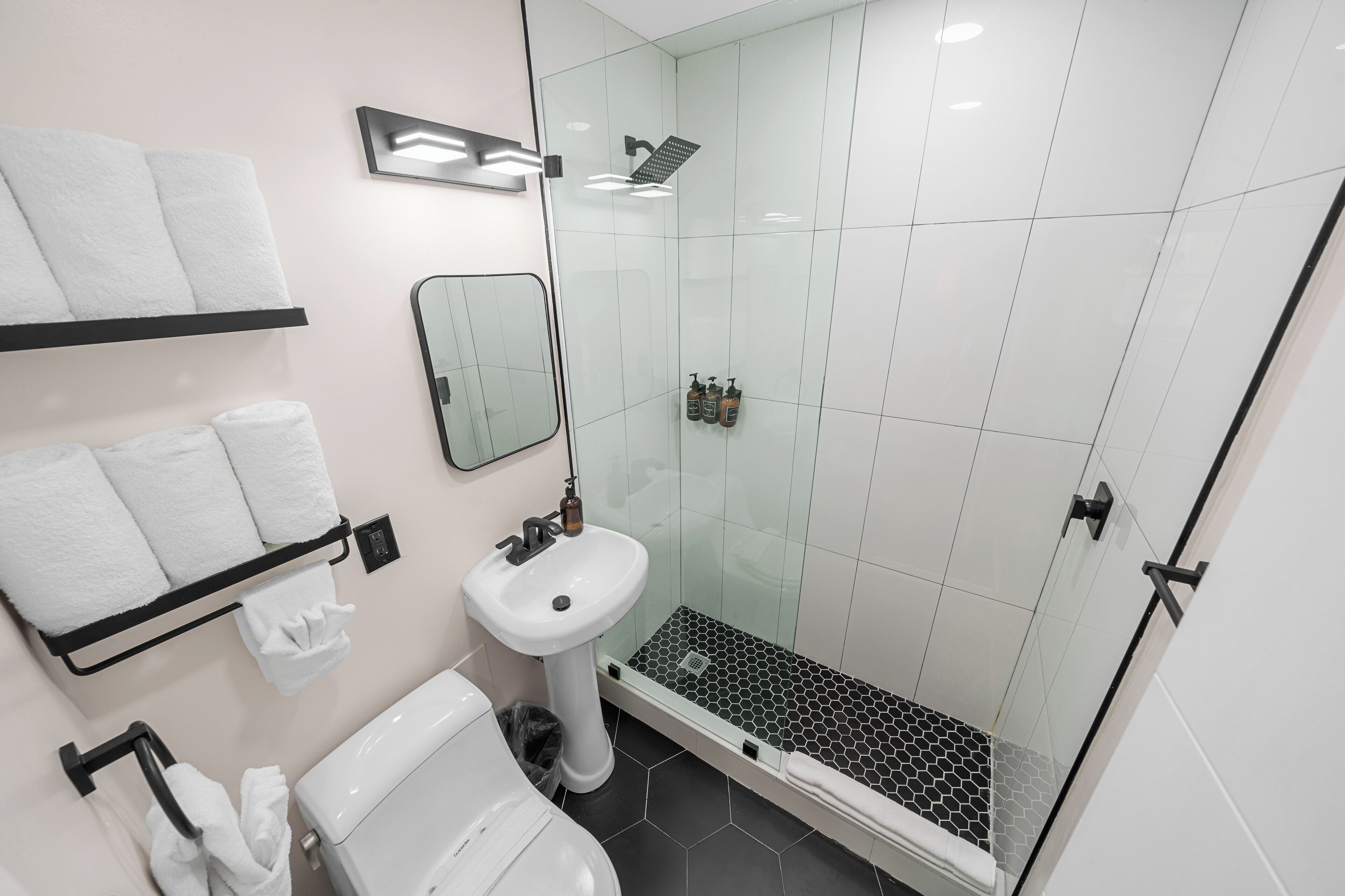 Ein modernes Badezimmer mit einer gläsernen Dusche, einem weißen Waschbecken auf Säule und einer Toilette.