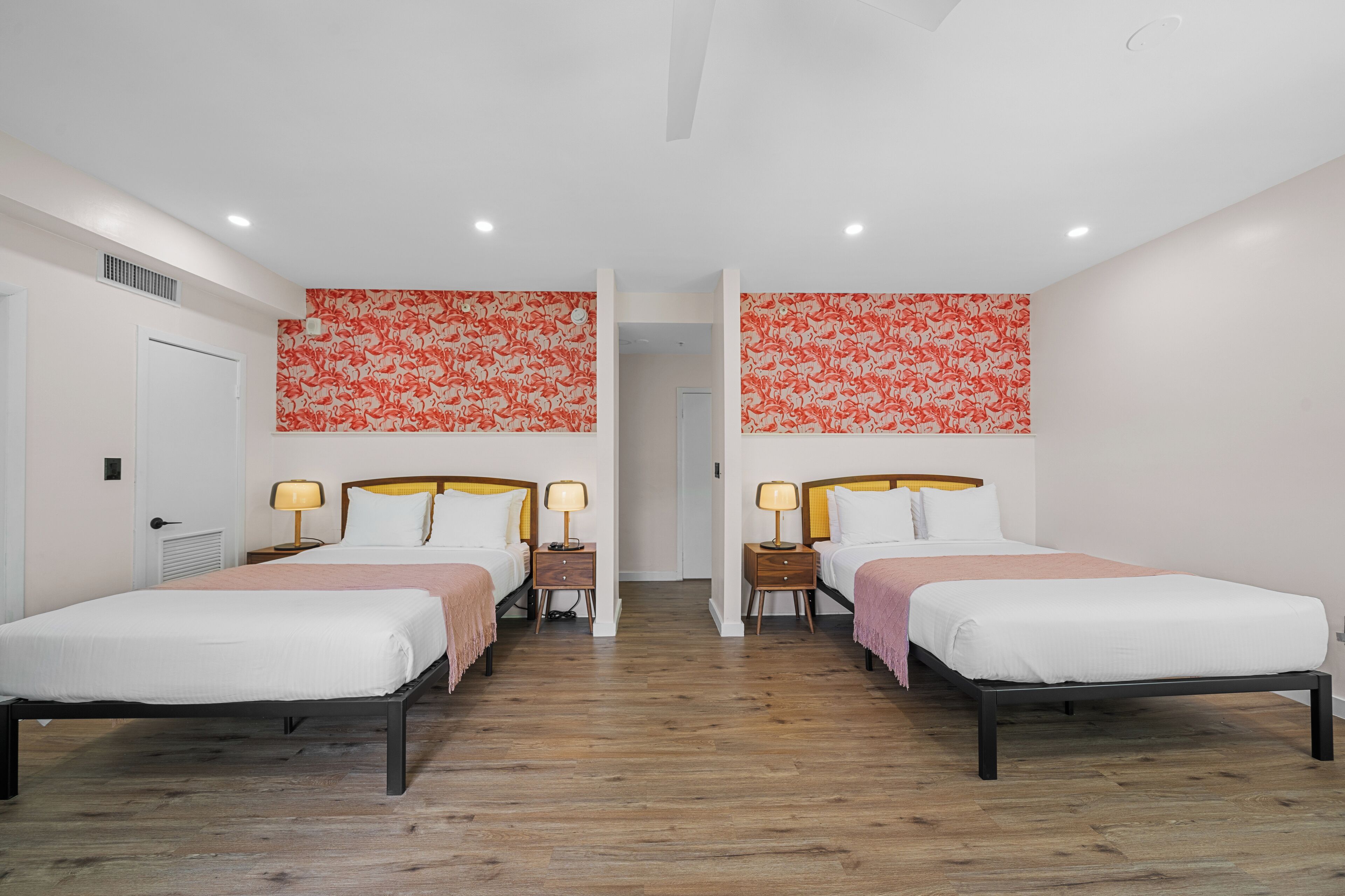 A hotel room with two single beds, wooden flooring, a white door, and a red floral wall design.