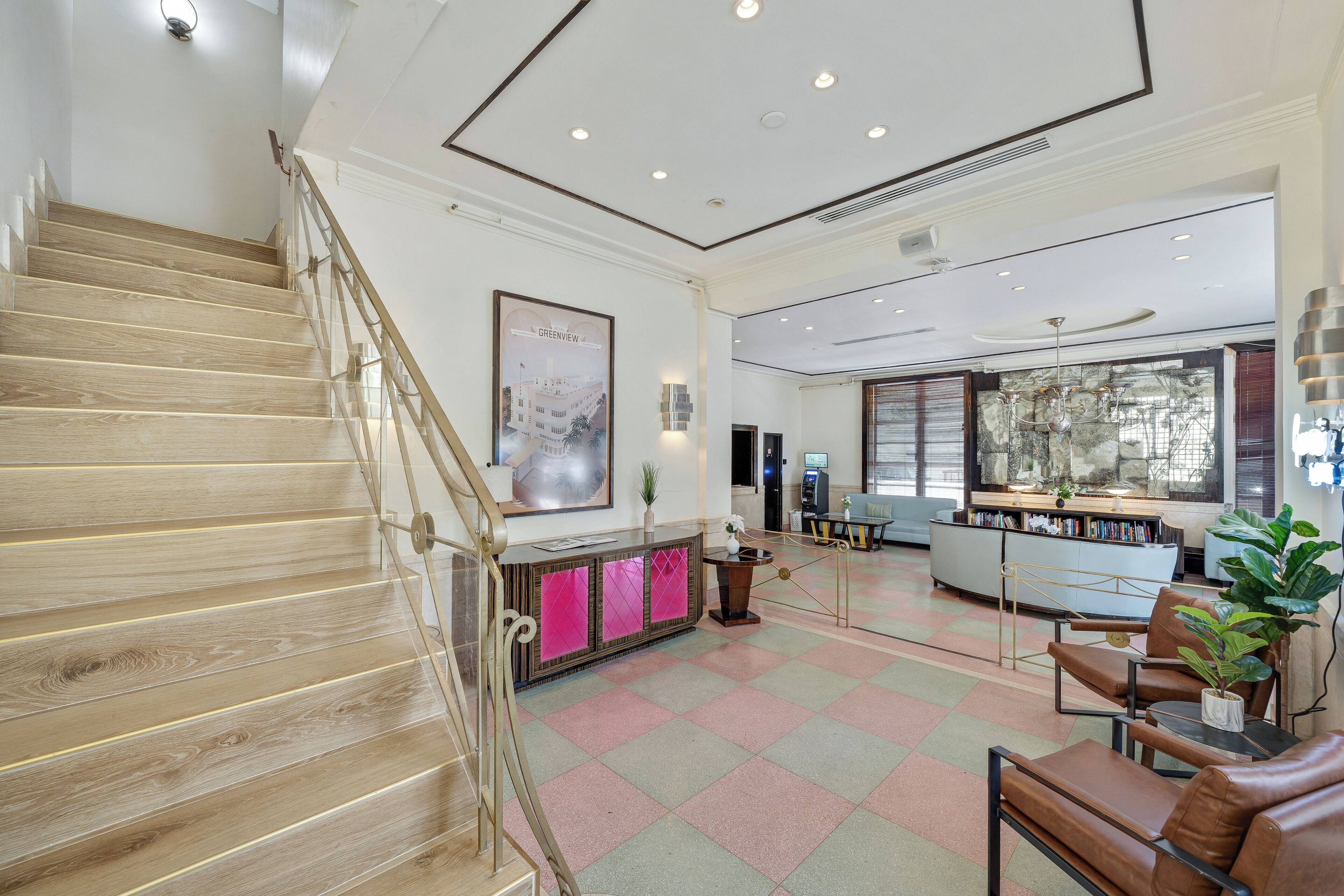 Un vestíbulo de hotel con una escalera de madera, una recepción, zona de estar y un ventanal grande.
