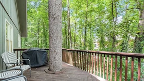Eine Holzdielen-Terrasse mit überdachtem Grill und zwei Stühlen, umgeben von einem Hollerdgeschoss und dichtem Grün.