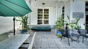 Eine Terrasse mit einem grünen Sonnenschirm, einer Bank und zwei Stühlen. Ein Schild zeigt die Aufschriften "GREENVIEW LOWKL" und "UNERLÄSSTLICHER EINGANG VERBOTEN".
