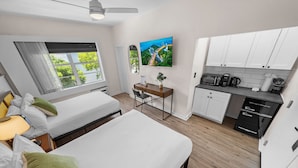 Ein modernes Hotelzimmer mit zwei Betten, einem Schreibtisch, einem Fernseher und einer Küchenzeile.