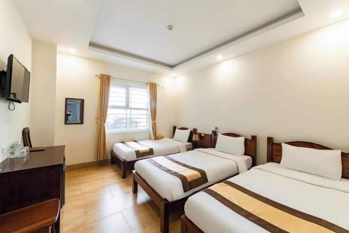 Une chambre d’hôtel avec trois lits, un bureau, une télévision et une fenêtre avec des rideaux.