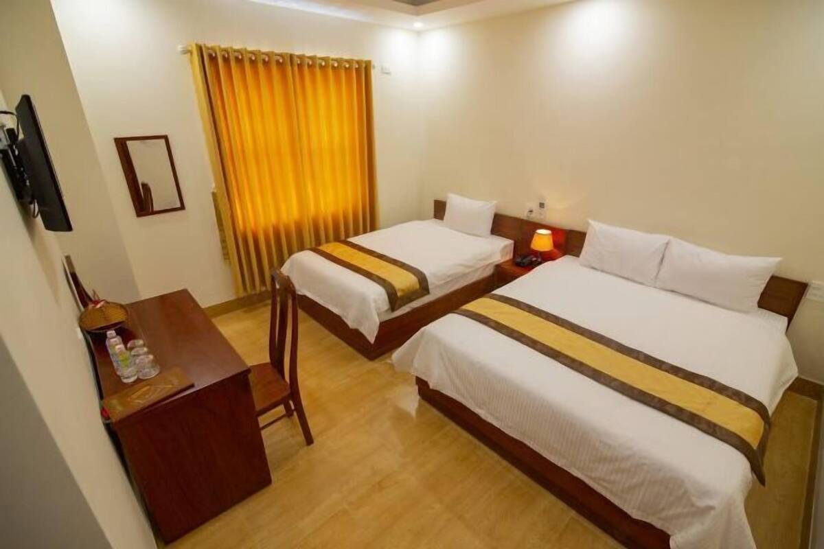 Une chambre d’hôtel avec deux lits, un bureau, une chaise, une télévision et un rideau.